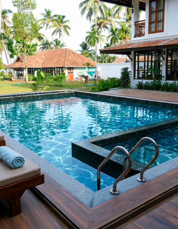 Sanskreti pool and shallow kids' pool bordered by loungers under coconut palms, overlooking the backwaters