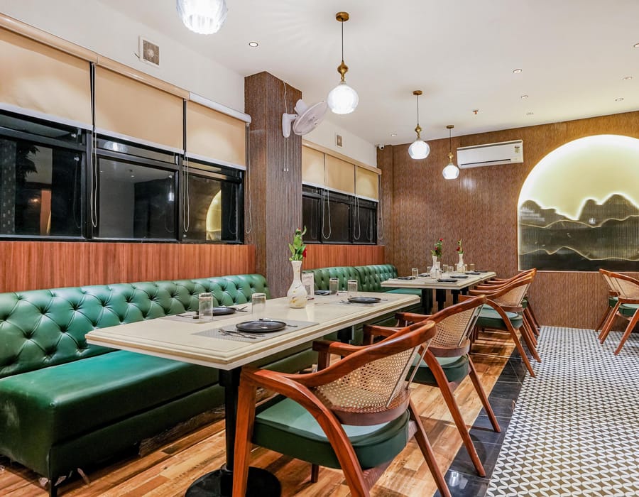 The Restaurant at Aura Bliss, with a green tufted banquette running along tables and wooden chairs, below pendant lights