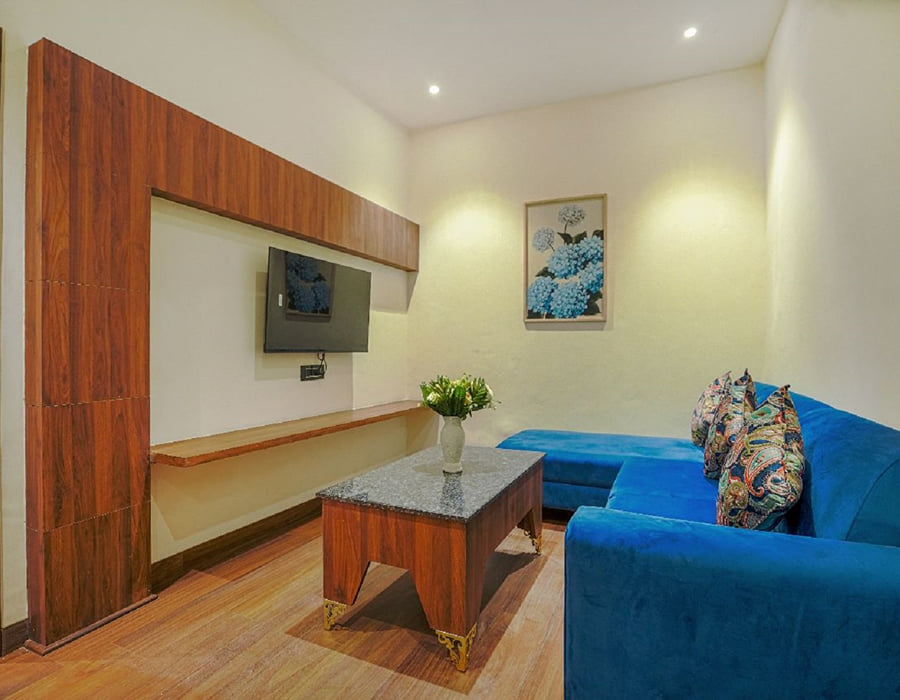 The living area of a Suite at Escala Hotel, with a blue sofa, a wall-mounted television on the timber panel