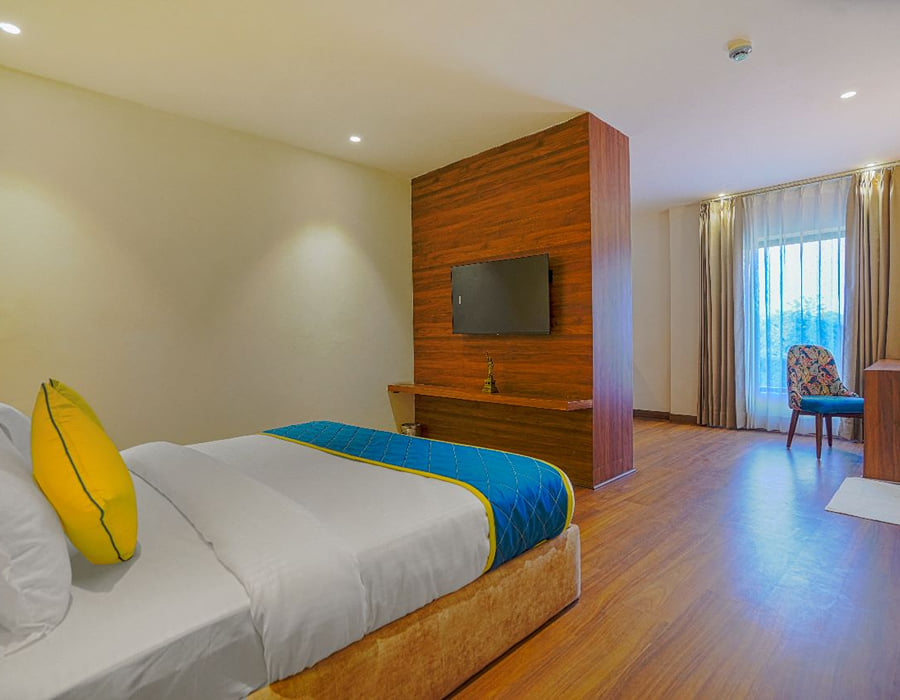 A Suite at Escala Hotel, with a wall-mounted television on a timber panel facing the bed and a curtained window