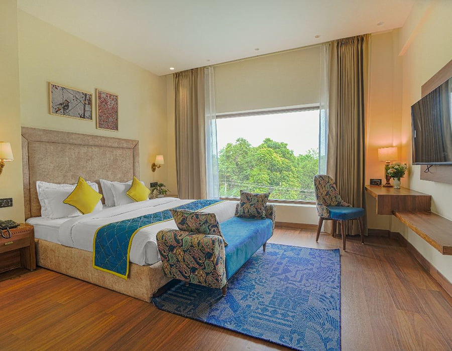A Super Deluxe room at Escala Hotel, with a blue bed runner, a patterned armchair, a television opposite