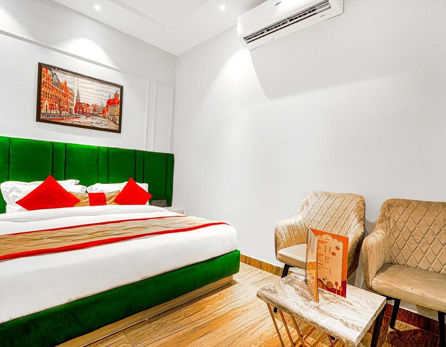 A Deluxe room at Grand Cabbana, with a green padded headboard, red and white bedding, two beige armchairs and framed artwork