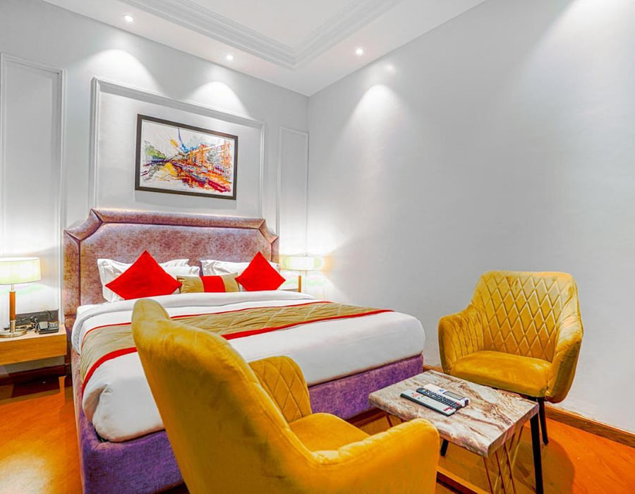A Super Deluxe room at Grand Cabbana, with a mauve bed base, two yellow armchairs and a small side table on the wooden floor