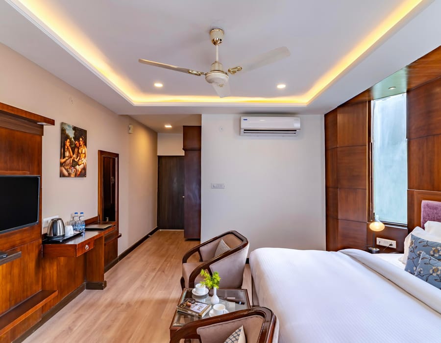 A Super Deluxe room at Hotel Karnika, with a television opposite the bed, a desk set with a kettle