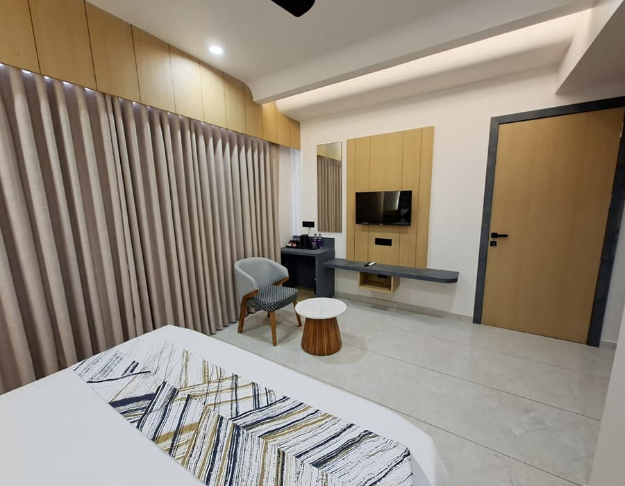 A guest room at Hotel Shree Radhe By White Panda, with a television on the timber panel opposite the bed, an armchair