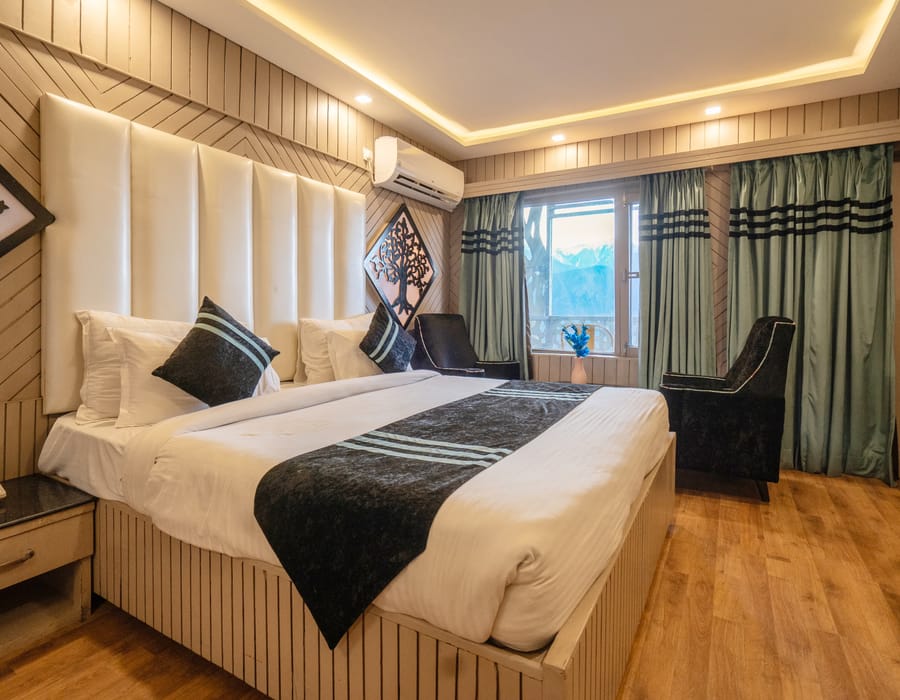 A King room with balcony at Levelup The Heritage Kud, with a tall padded headboard, timber panelling and armchairs