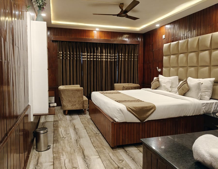 A Queen room at Levelup The Heritage Kud, with dark timber panelling, a padded headboard, armchairs in the corner