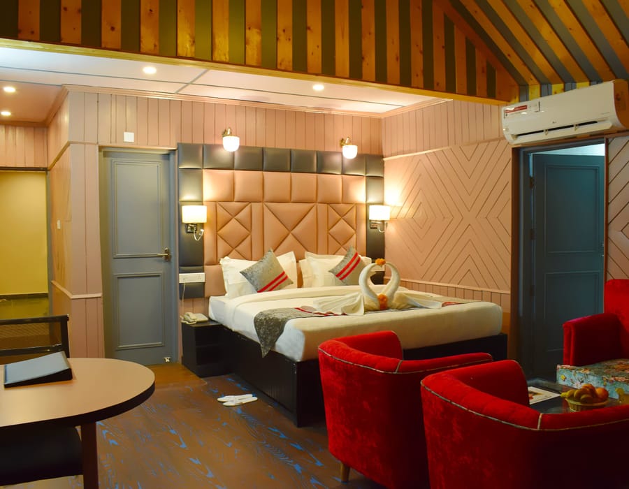A Family room at Levelup The Heritage Kud, with a padded headboard, two red armchairs drawn up to a table