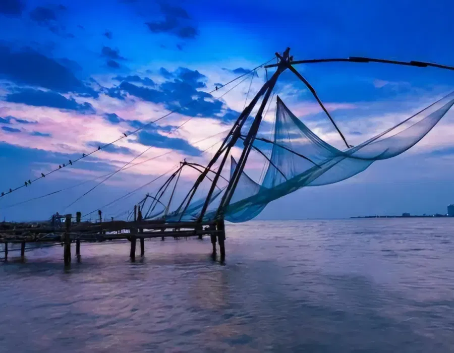 Row of cantilevered Chinese fishing nets silhouetted against an orange sky at sunset on the Fort Kochi waterfront