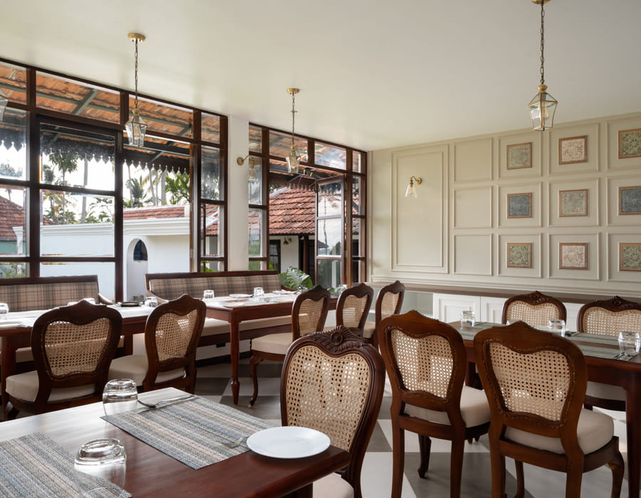 The Lilly's dining room with a framed gallery wall, upholstered chairs and wooden tables set for a meal, Sanskreti, Kumbalanghi