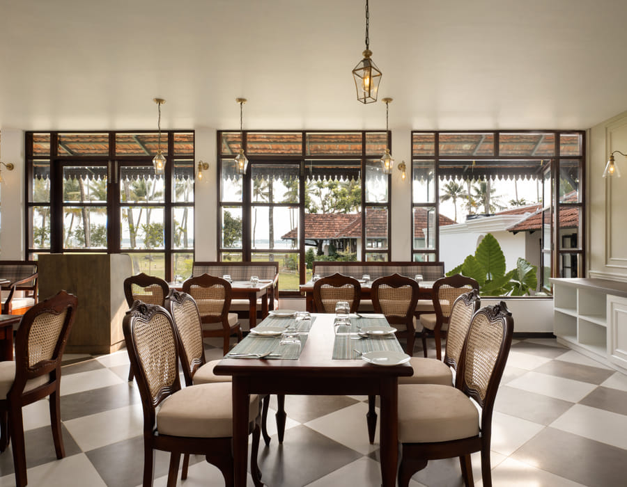 Cane sofa seating and low wooden tables at The Lilly's with lake-side windows behind, Sanskreti, Kumbalanghi