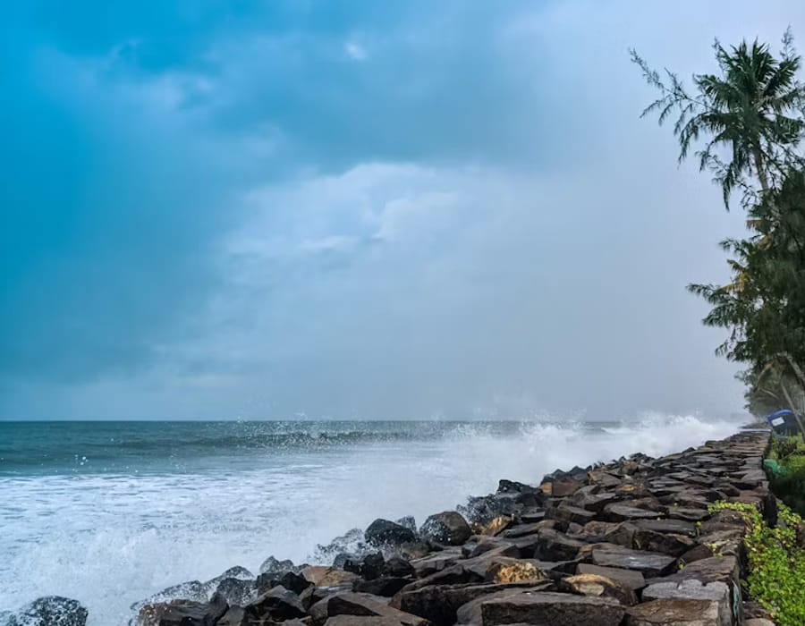 Marine Drive seafront promenade in Ernakulam with waves lapping a stone wall and city skyline beyond, Kochi
