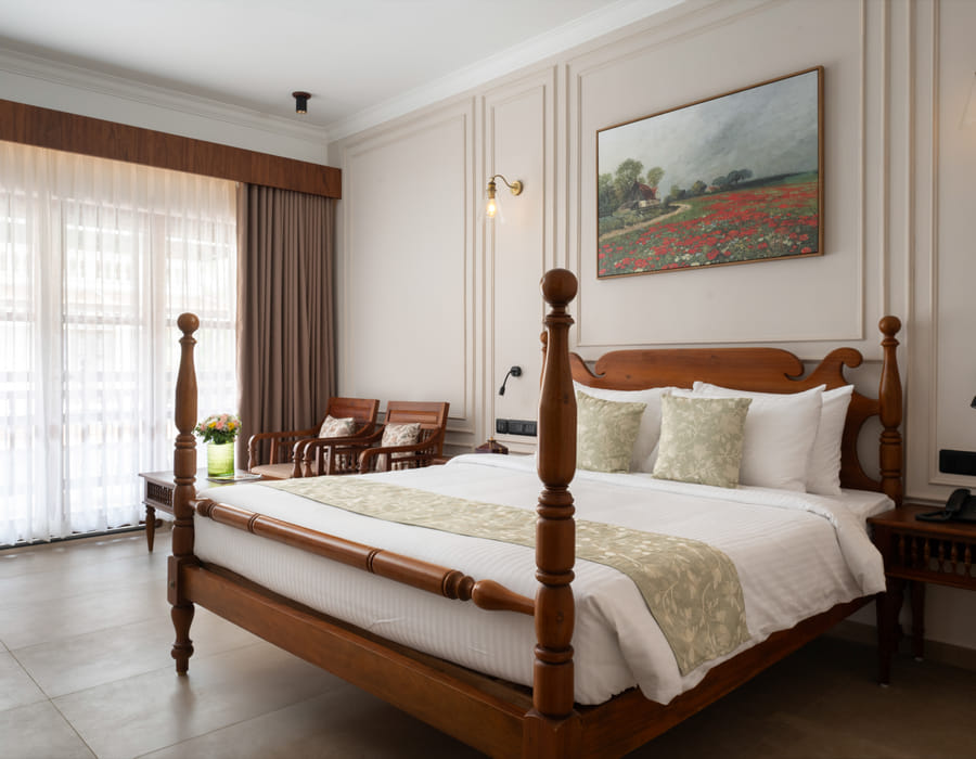 Pool View Room four-poster king bed with cane headboard and open balcony doors framing tropical greenery