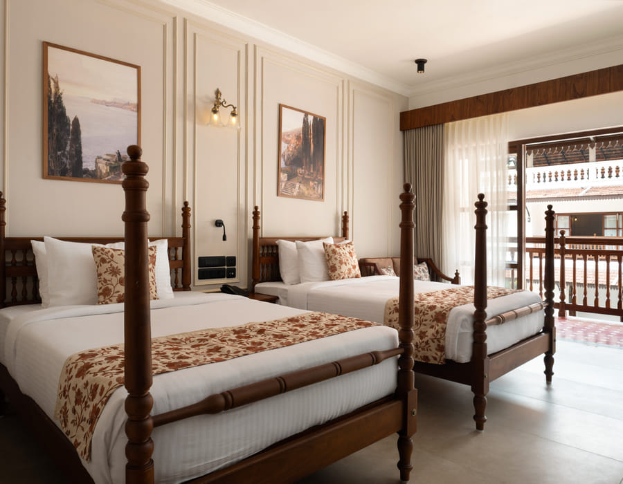 Pool View Twin Room with two four-poster twin beds, floral runners and pool-side balcony doors behind