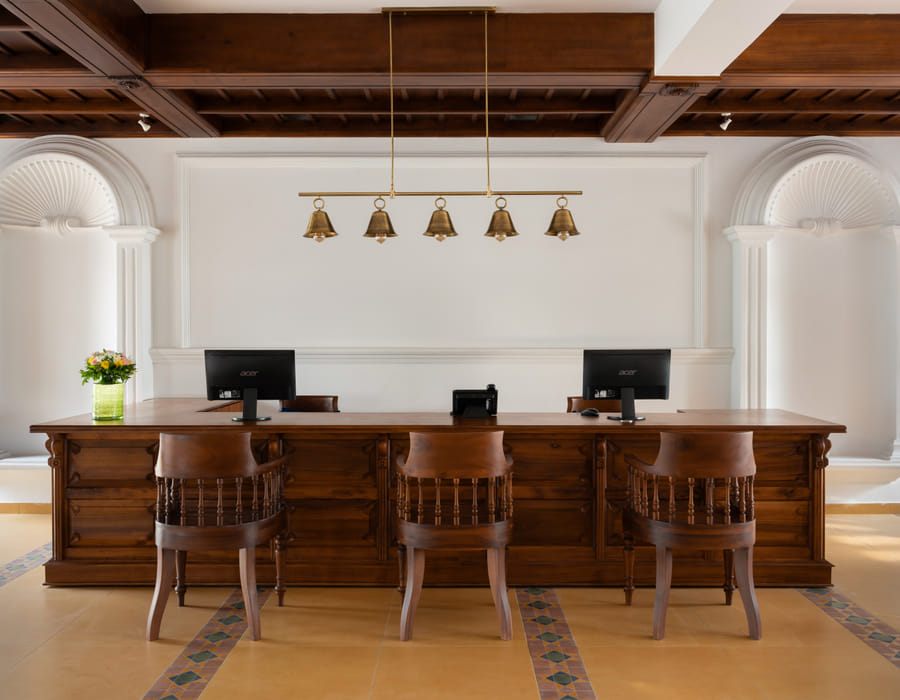 Sanskreti front desk with a carved wooden counter, brass lamps and floral arrangement on the reception table
