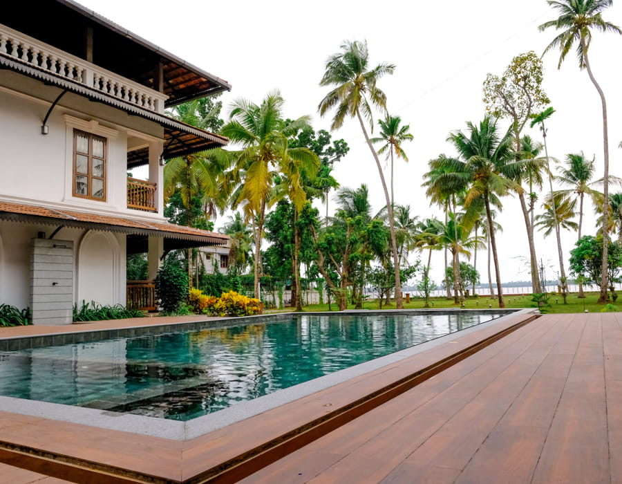 Sanskreti infinity pool aligned with the Vembanad backwaters, flanked by coconut palms and lounge chairs