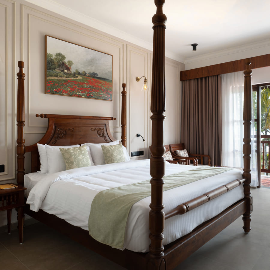 Lake View Room four-poster king bed with balcony doors opening onto palms and Vembanad Lake, Sanskreti