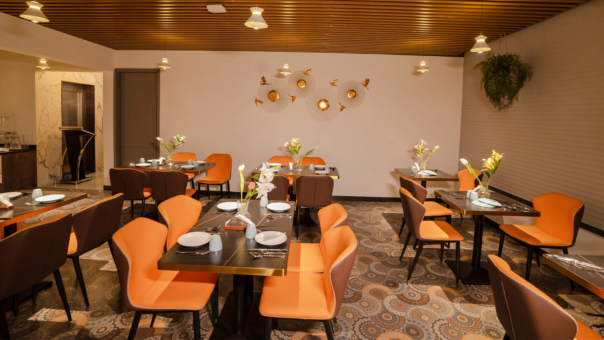 Dining hall with orange chairs, decorative wall discs, and a view toward the lift lobby