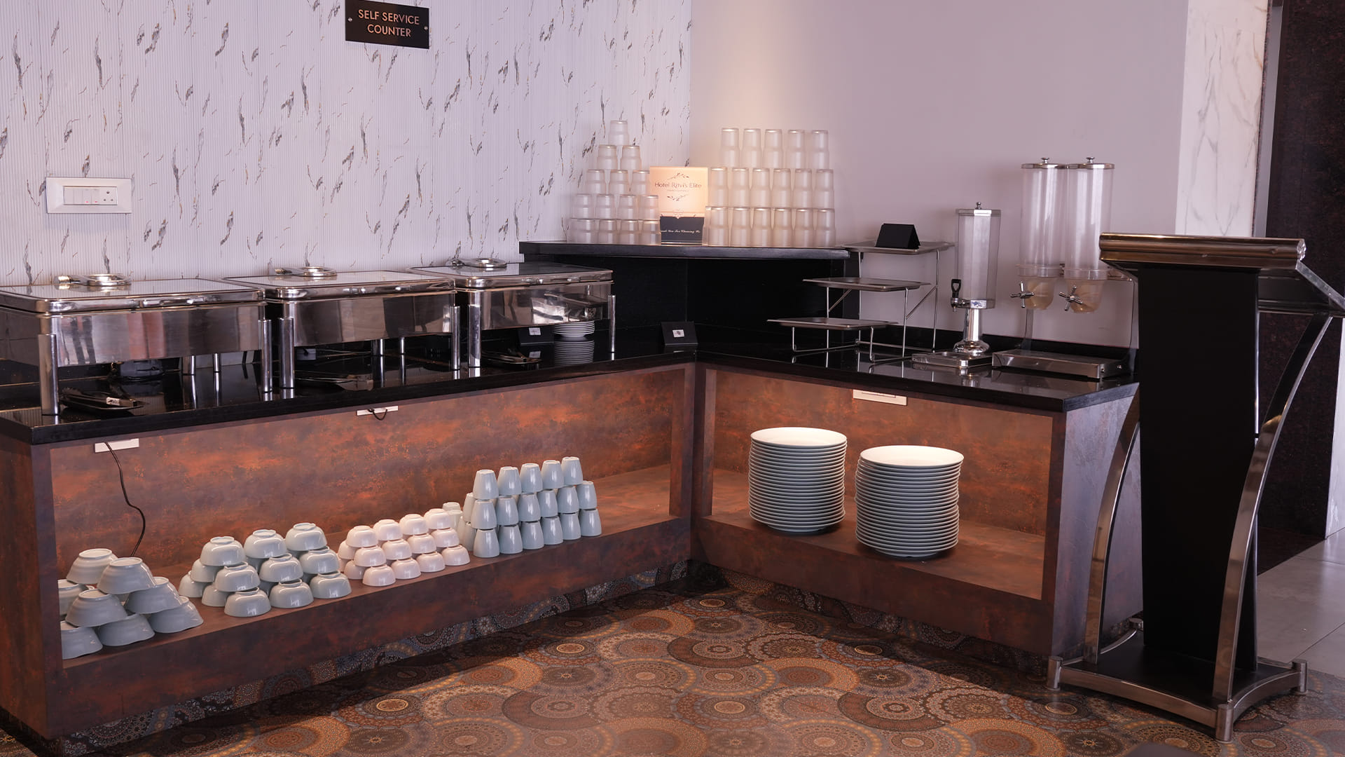 Self-service breakfast counter with chafing dishes, stacked plates and bowls, and disposable cups