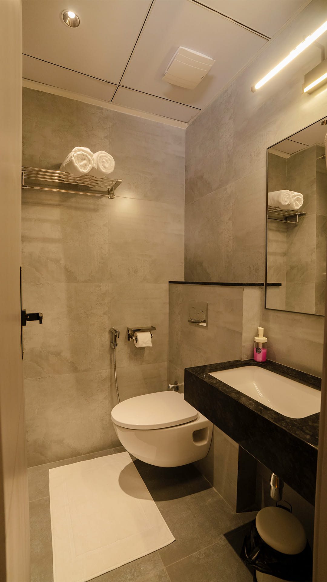 Bathroom with a wall-mounted toilet, a floor mat, and a black granite vanity