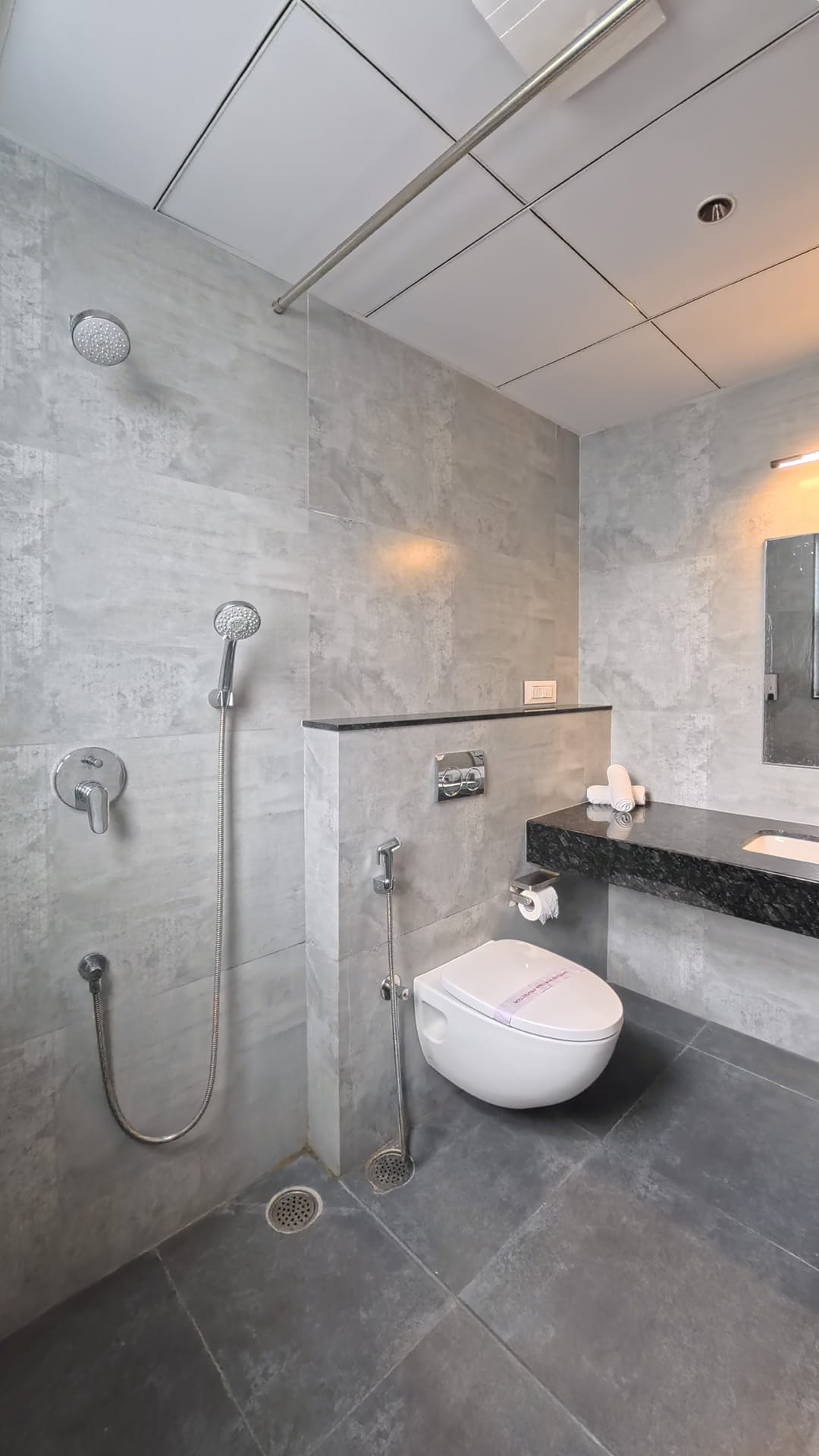 Bathroom with an open rain shower, a handheld sprayer, and a wall-mounted toilet