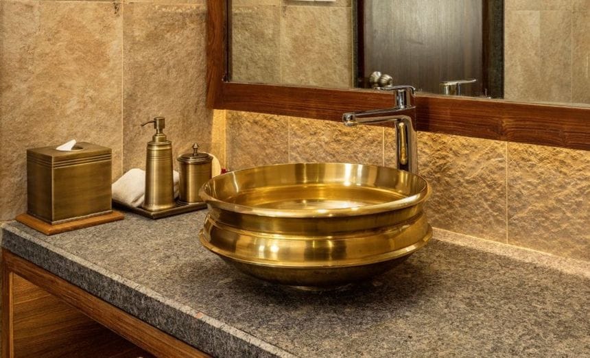A brass basin beside a soap dispenser and toiletries on a bathroom counter at Nepali Ghar Hotel, part of its programme to reduce single-use plastic bottles.
