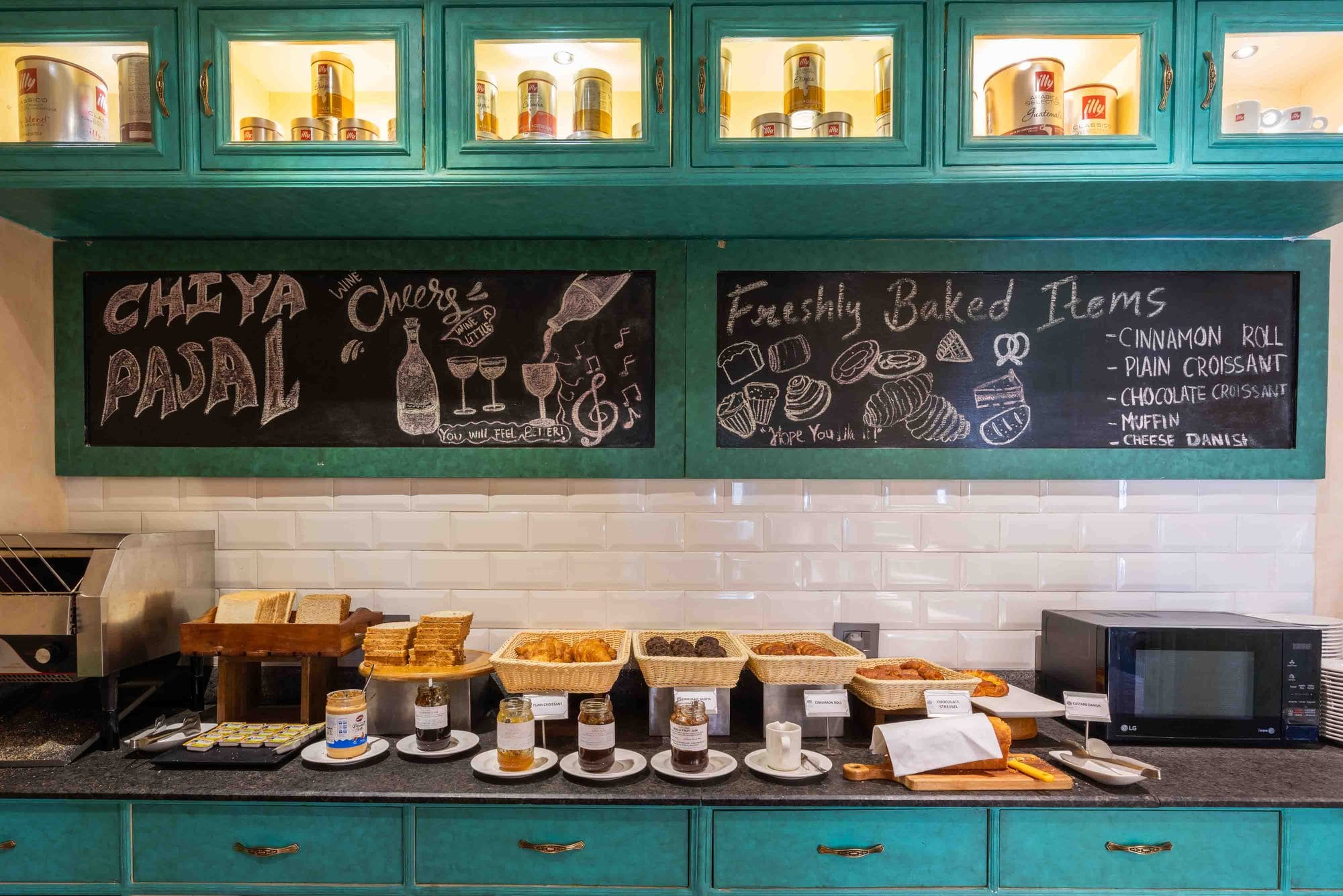 The counter at Chiya Pasal, the all-day dining restaurant of Nepali Ghar Hotel, its hand-chalked board listing freshly baked items above the teal cabinetry.