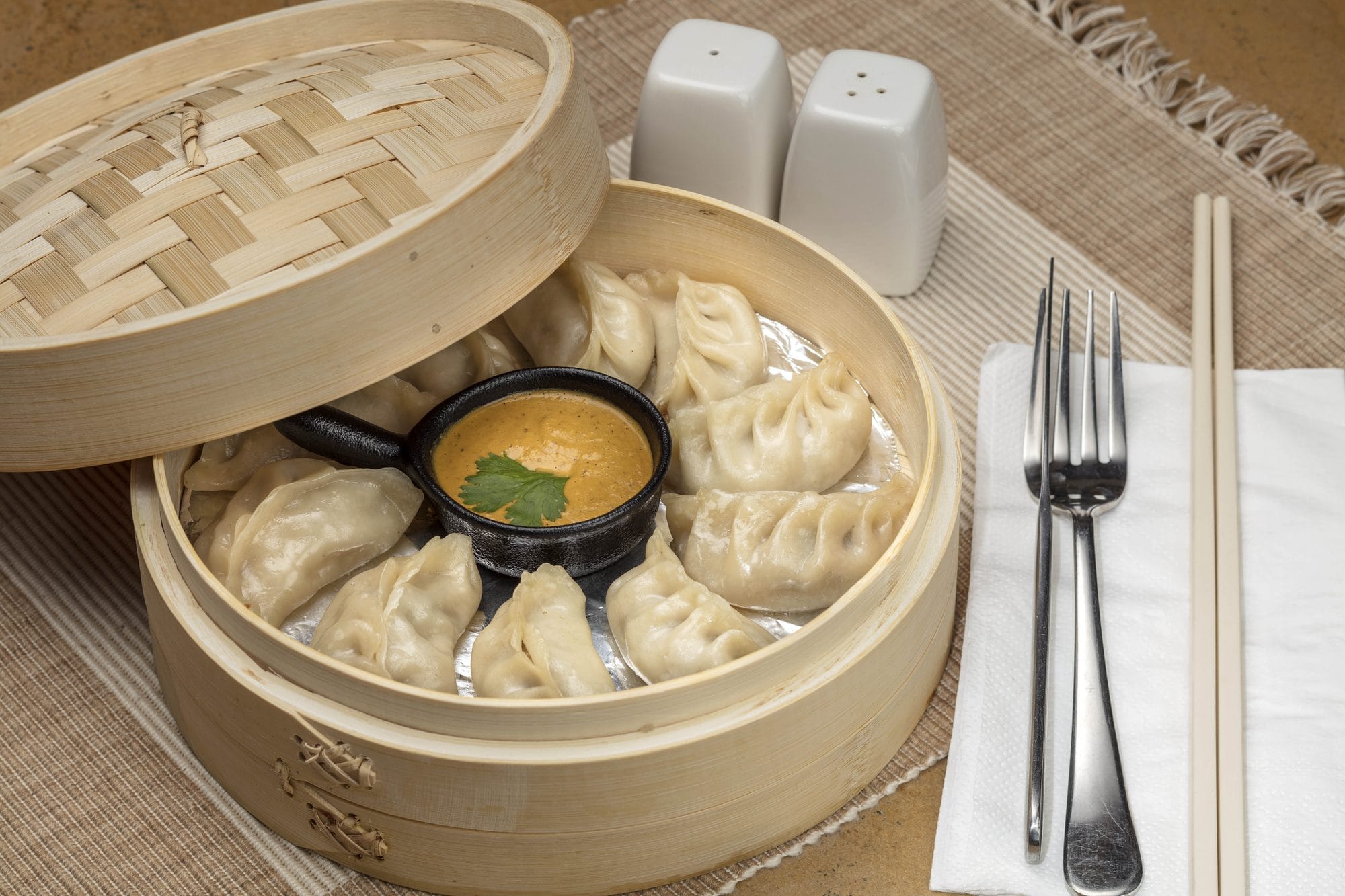 Steamed Mo:Mo, a signature dish at Chiya Pasal restaurant, Nepali Ghar Hotel, served in a bamboo steaming basket alongside a small bowl of spicy dipping sauce.