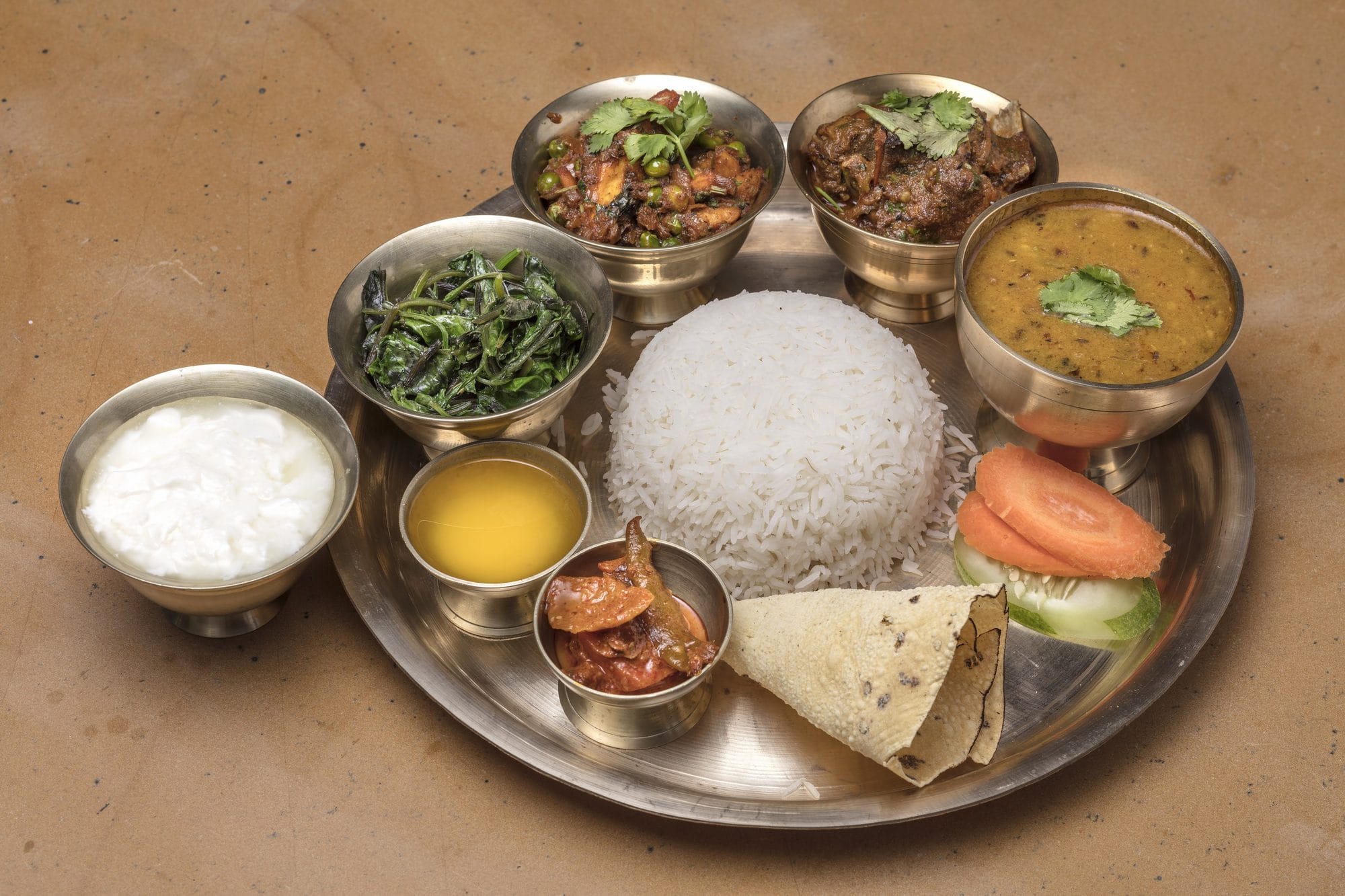 A Nepali Thali Set, a signature dish at Chiya Pasal restaurant, Nepali Ghar Hotel, served on a brass platter with curries, rice, and traditional accompaniments.