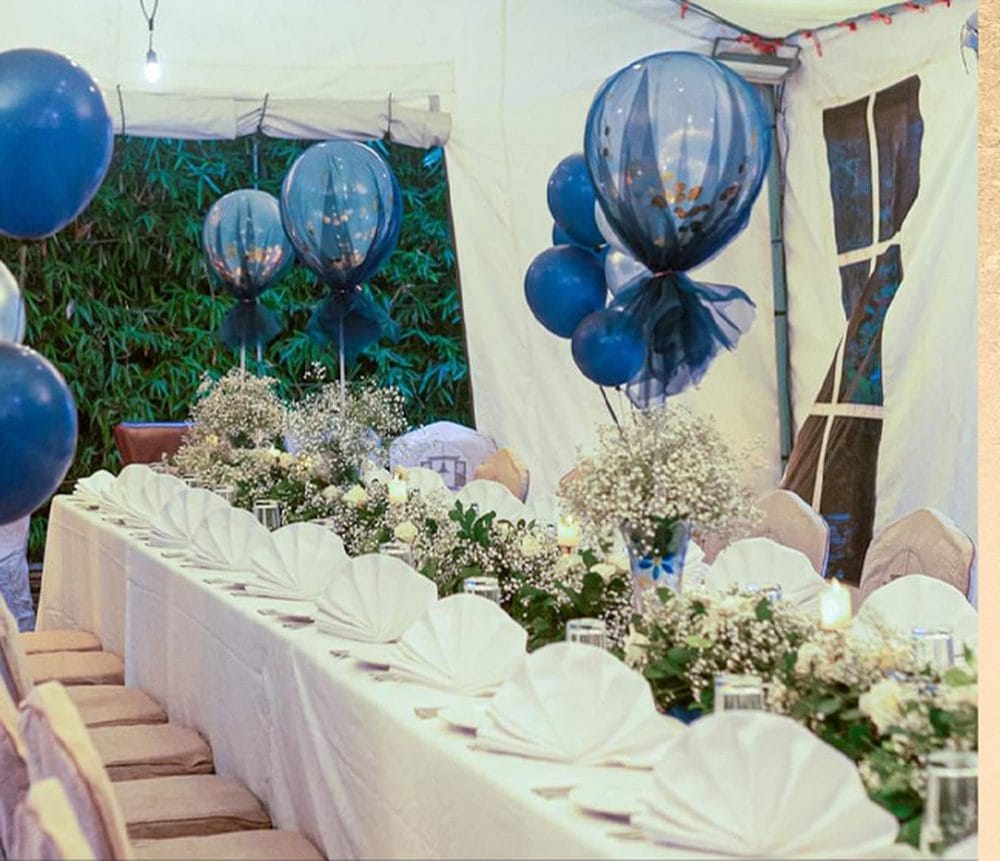 A private party table setting in the garden at Nepali Ghar Hotel, dressed with navy tulle balloons, baby's breath flowers, and scalloped white folded napkins.