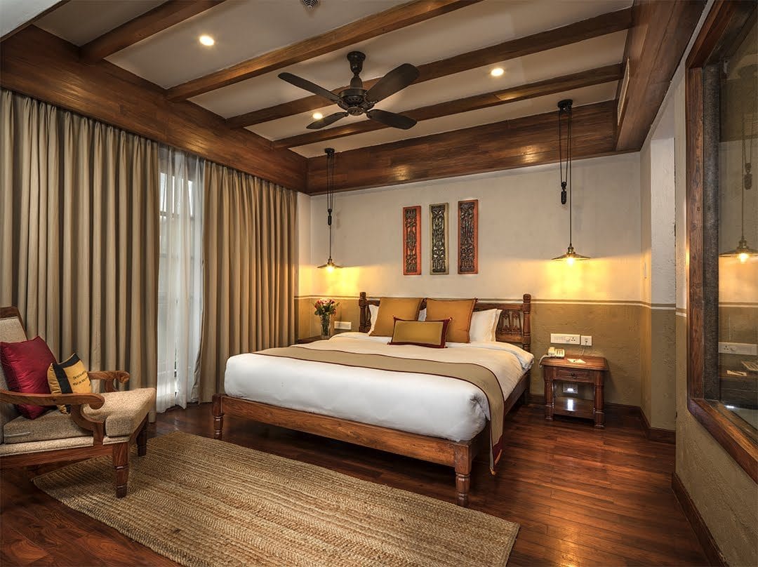 The Executive Suite bedroom at Nepali Ghar Hotel, its king-size bed framed by Newari wood panels and warm brass pendant lights hanging from the timber ceiling.