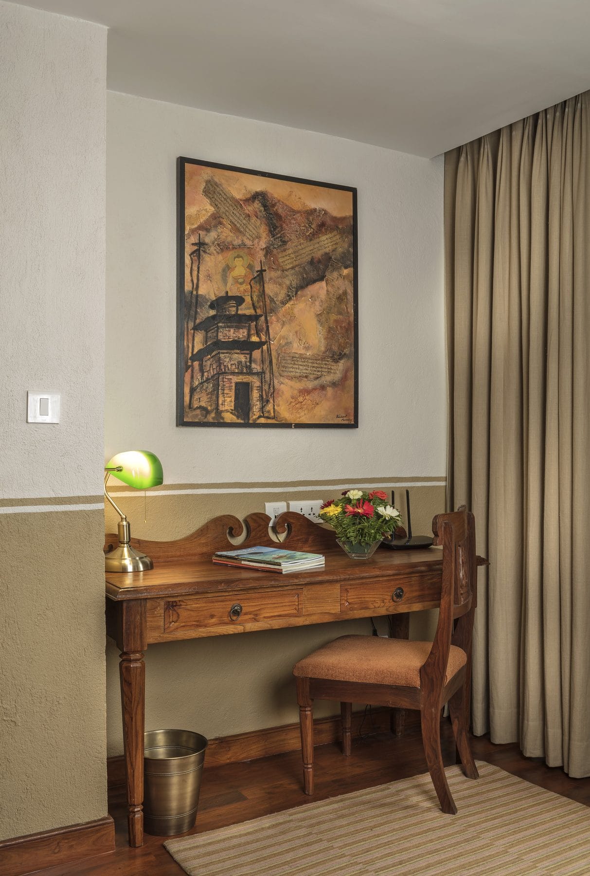 The writing desk in the Executive Suite at Nepali Ghar Hotel, positioned beneath a painting of a Newari temple and fitted with a small chair and a reading lamp.
