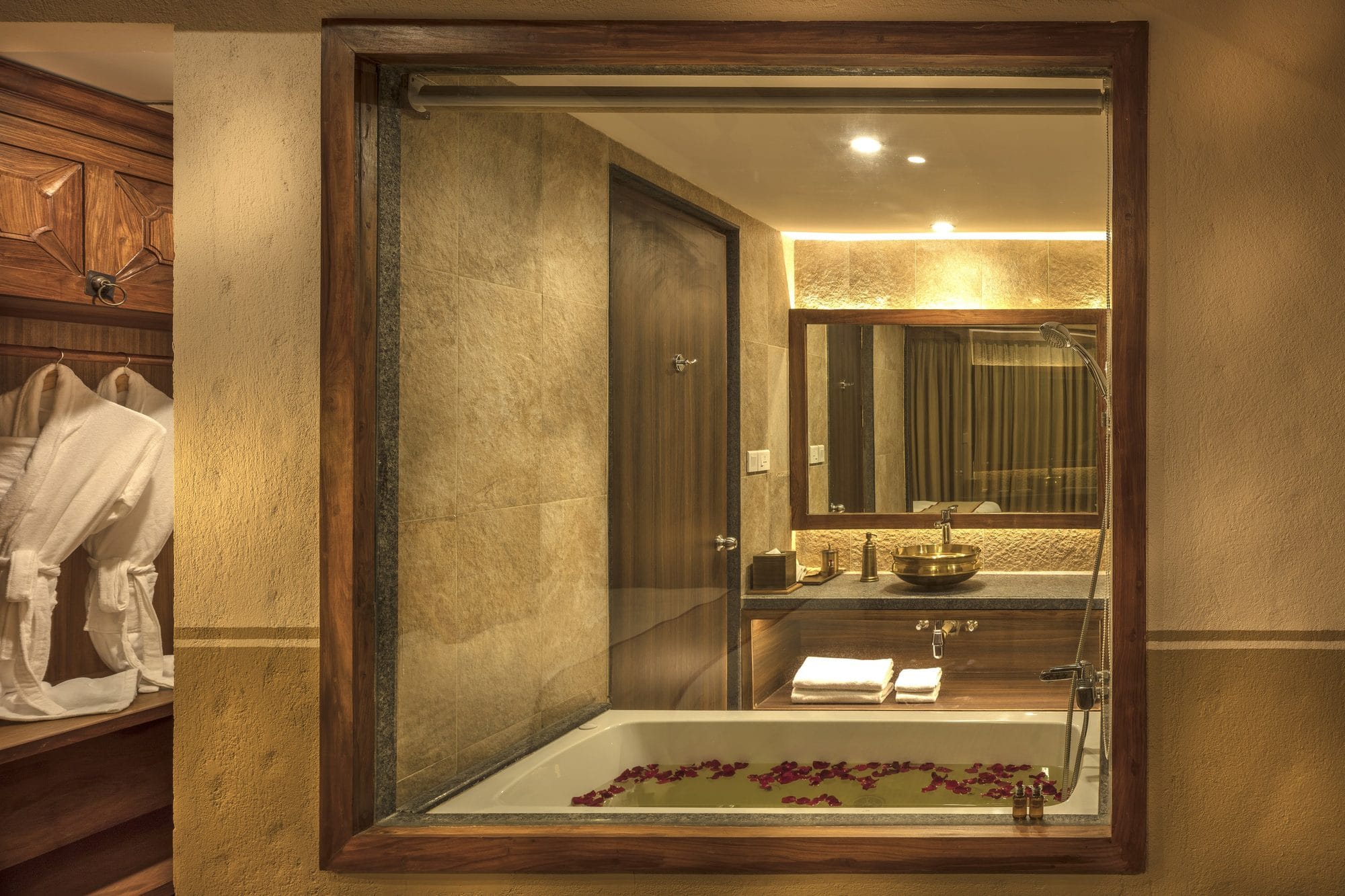 The Executive Suite Jacuzzi at Nepali Ghar Hotel, filled and set with white rose petals, seen through a carved timber window from the adjoining dressing area.