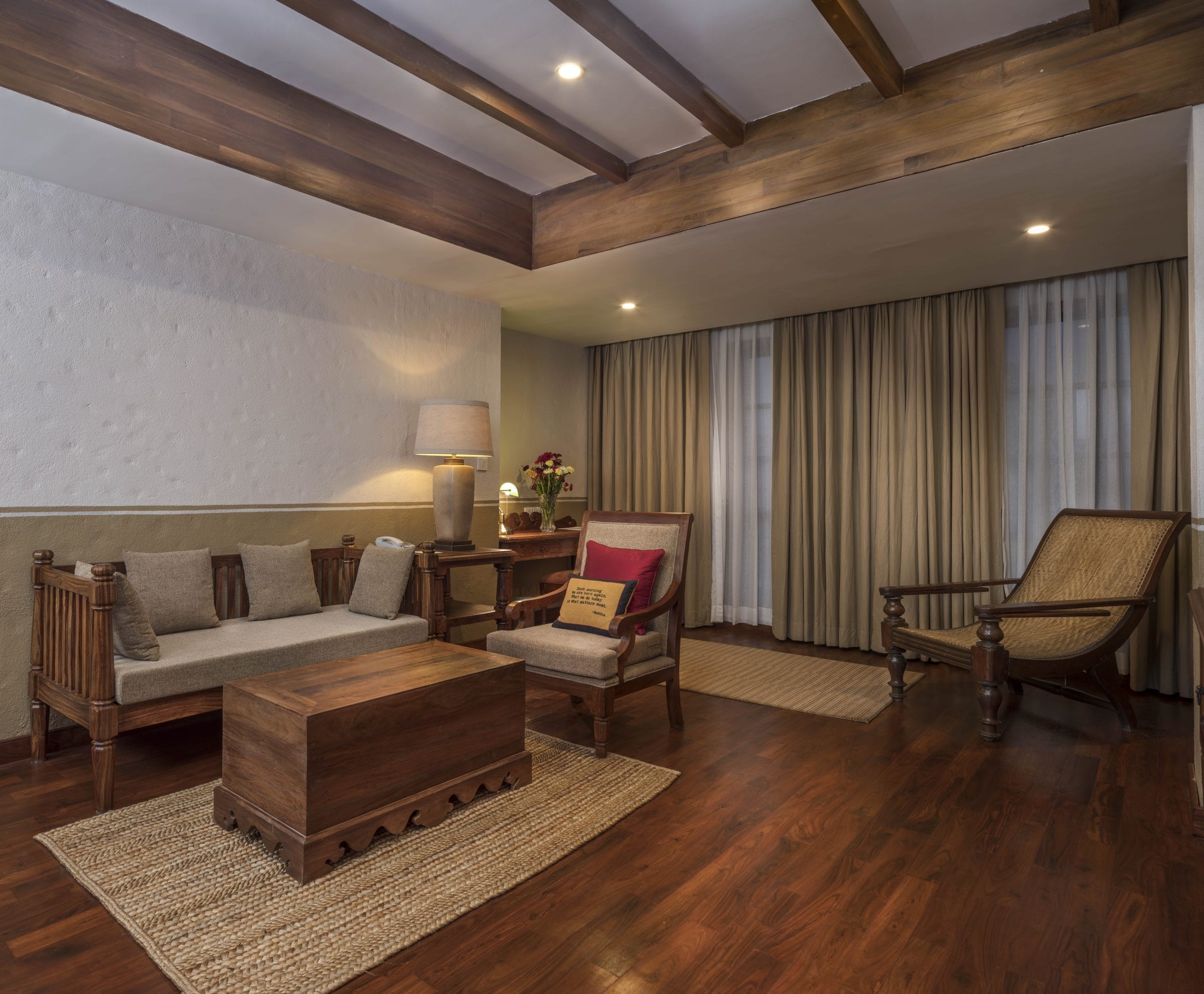 The separate living room of the Executive Suite at Nepali Ghar Hotel, with a timber-beamed ceiling, a daybed, and a caned rattan planter's chair by the window.