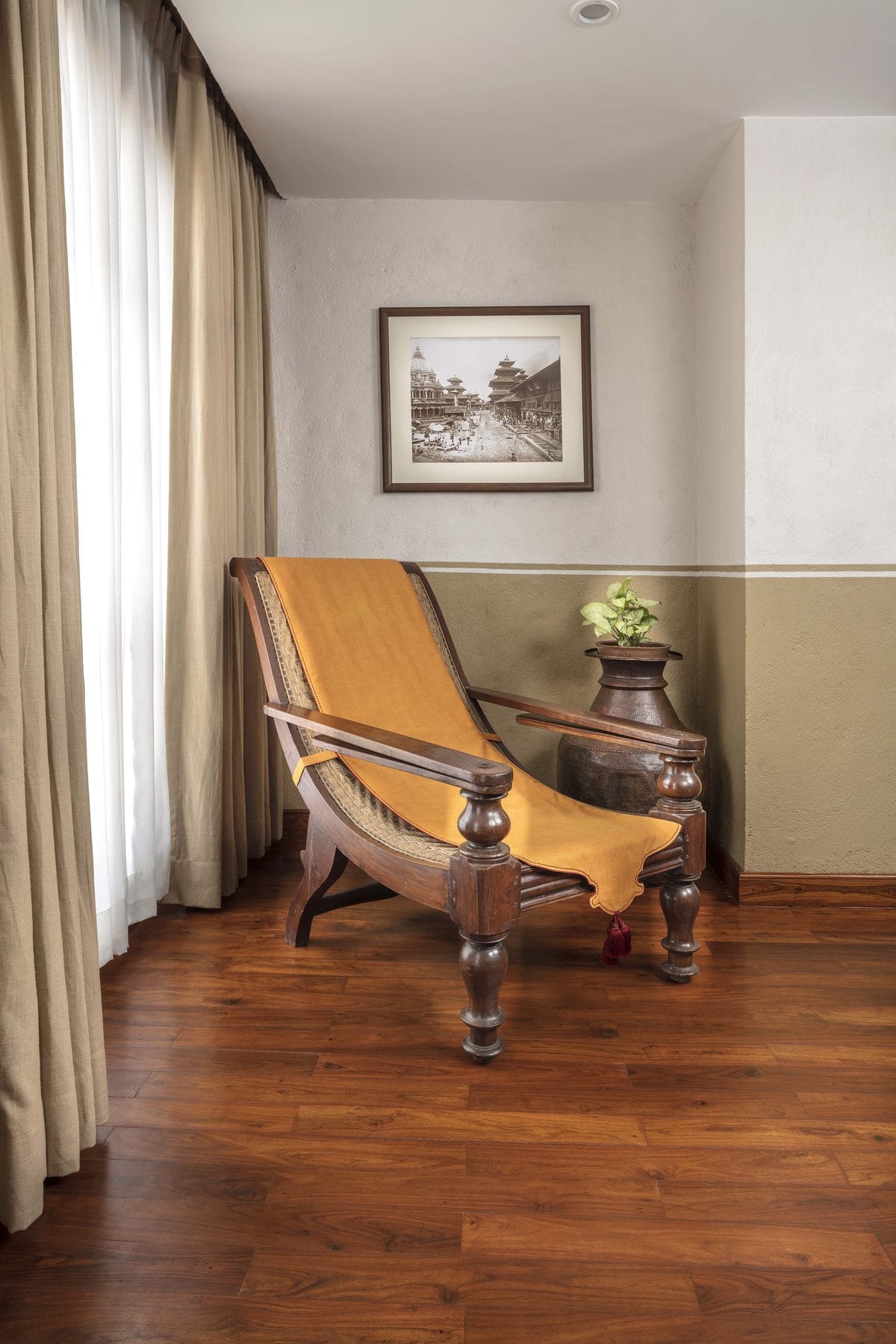 A caned planter's chair positioned by the window of the Executive Suite at Nepali Ghar Hotel, beside an archival photograph of the old Kathmandu city streets.