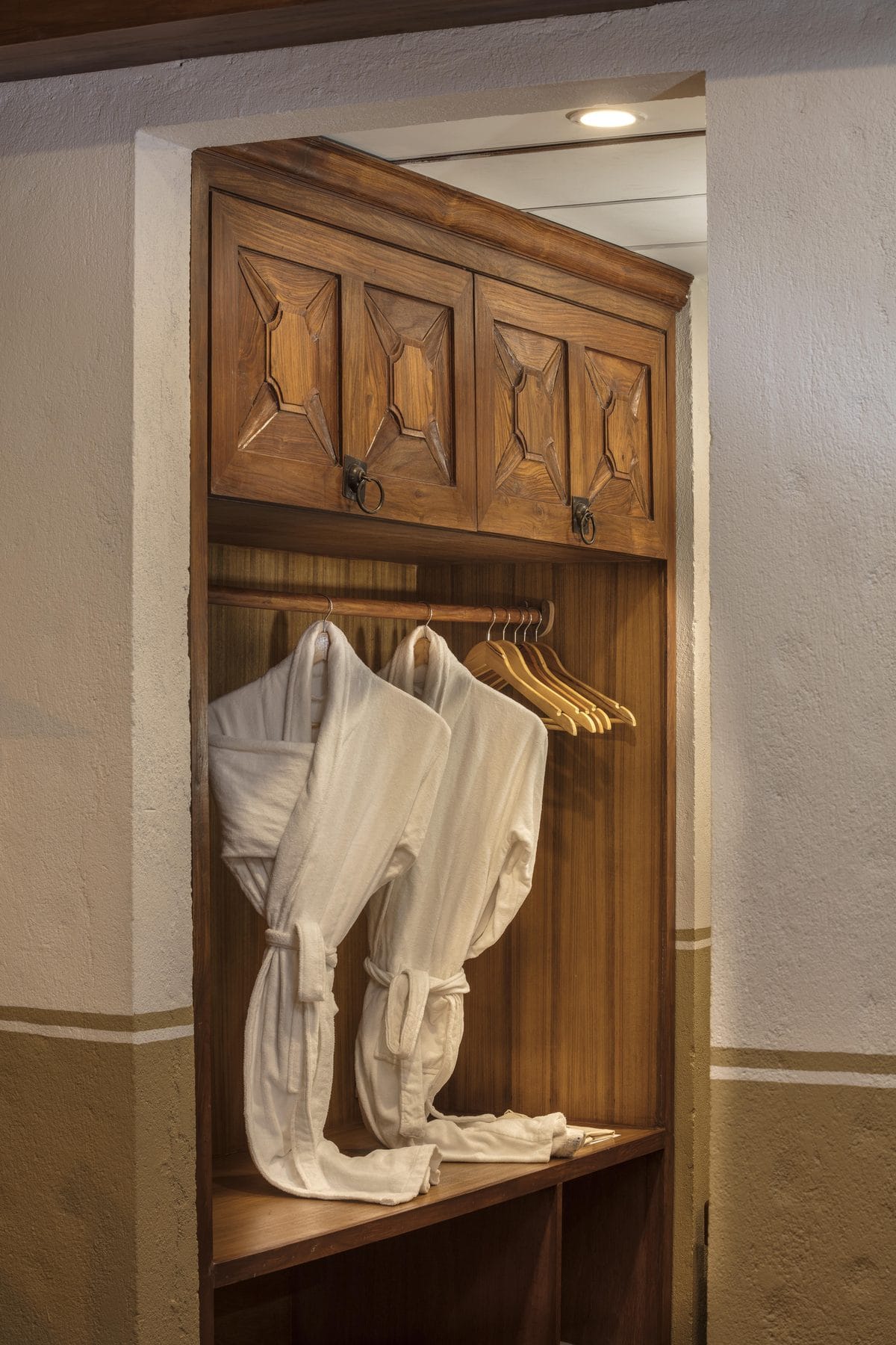The carved timber wardrobe of the Executive Suite at Nepali Ghar Hotel, its doors hung inside with white bathrobes ready for guests to use during their stay.