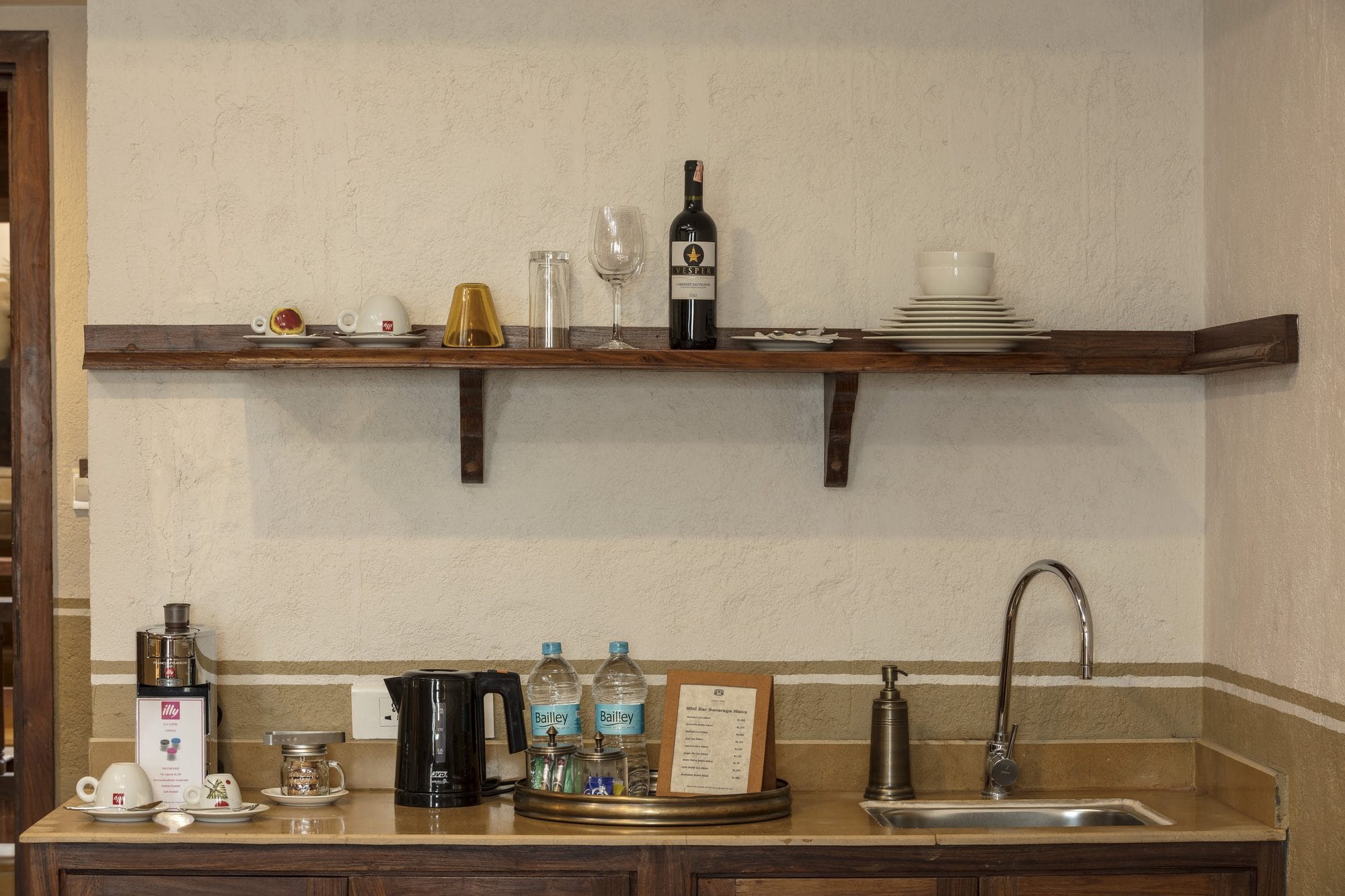 The Executive Suite pantry at Nepali Ghar Hotel, fitted with a coffee machine, an electric kettle, a minibar, and a shelf of glassware above the wooden counter.