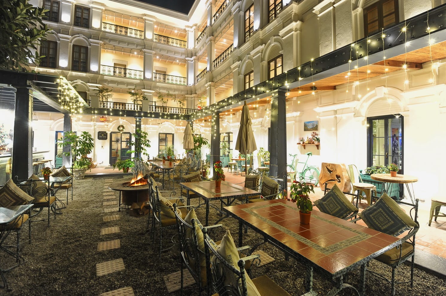 Garden seating beside the koi pond and waterfall in the front yard at Nepali Ghar Hotel at night, with string lights strung against the hotel's brick facade.