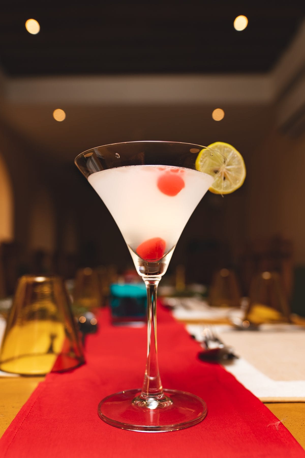 A martini garnished with a fresh lemon wheel and cherries on the counter at Jharana Bar, the outdoor cocktail bar of Nepali Ghar Hotel, lit softly at night.