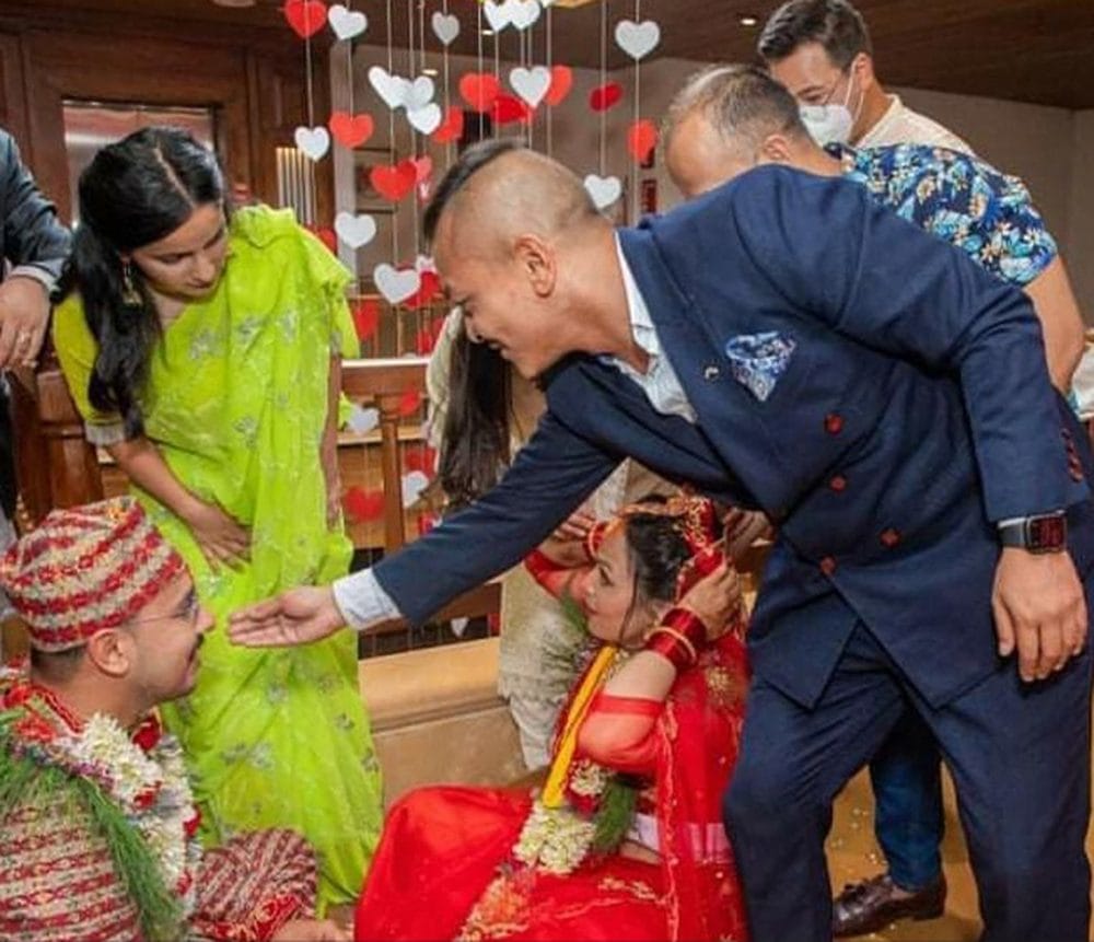 A Nepali bride and groom in wedding attire greeting a guest at a private reception hosted at Nepali Ghar Hotel, surrounded by red and white heart decorations.