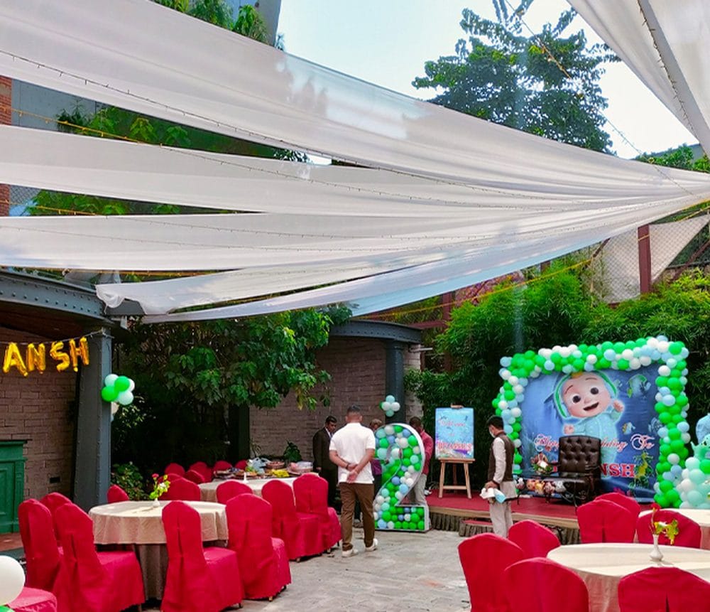 A birthday party set up in the garden courtyard at Nepali Ghar Hotel, with a balloon arch, red chair covers, and drapes strung overhead for the celebration.