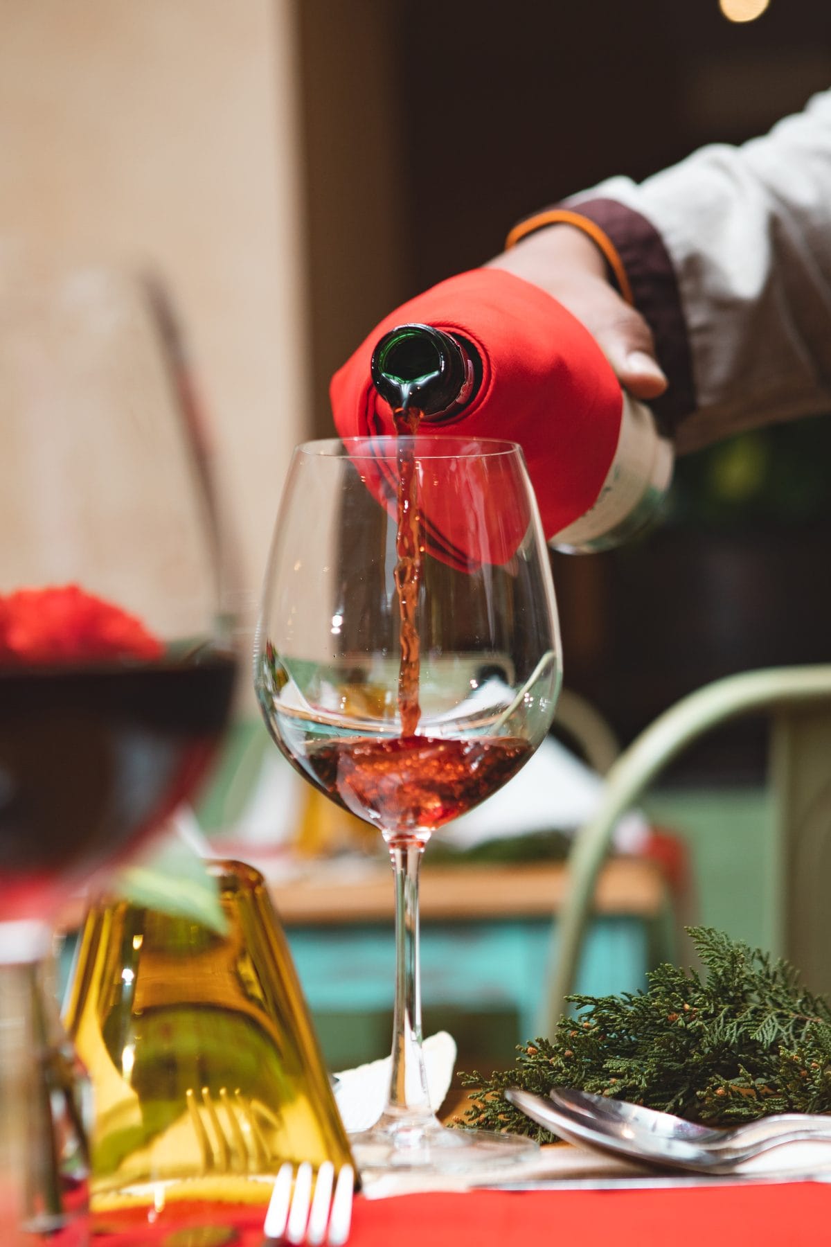 A server pouring red wine into a glass at Jharana Bar, the outdoor cocktail bar beside the koi pond and waterfall at Nepali Ghar Hotel in Thamel, Kathmandu.