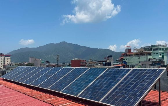 Rooftop solar panels installed at Nepali Ghar Hotel, seen against the Kathmandu skyline and surrounding hills nearby, part of its renewable energy initiatives.