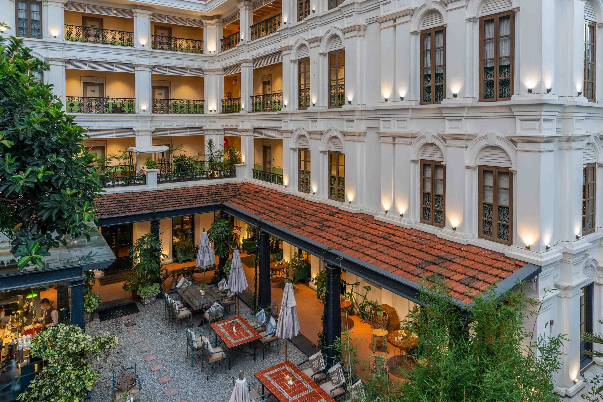An aerial view at dusk of the Seto Ghar courtyard at Nepali Ghar Hotel, its tiered balconies ringing a tiled colonnade lined with wrought-iron cafe tables.