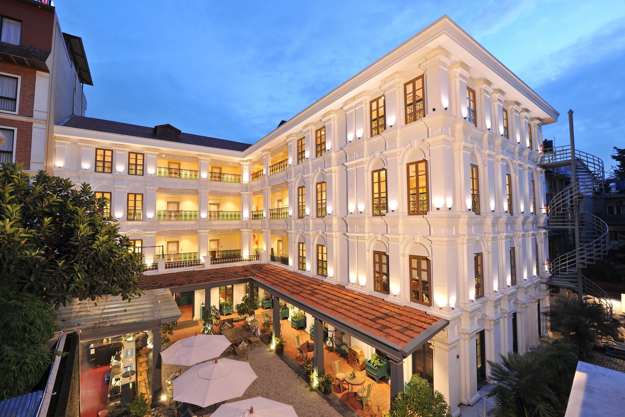 The whitewashed colonial facade of Seto Ghar, the Classical Wing of Nepali Ghar Hotel, with arched windows and wrought-iron balconies lit warmly at blue hour.