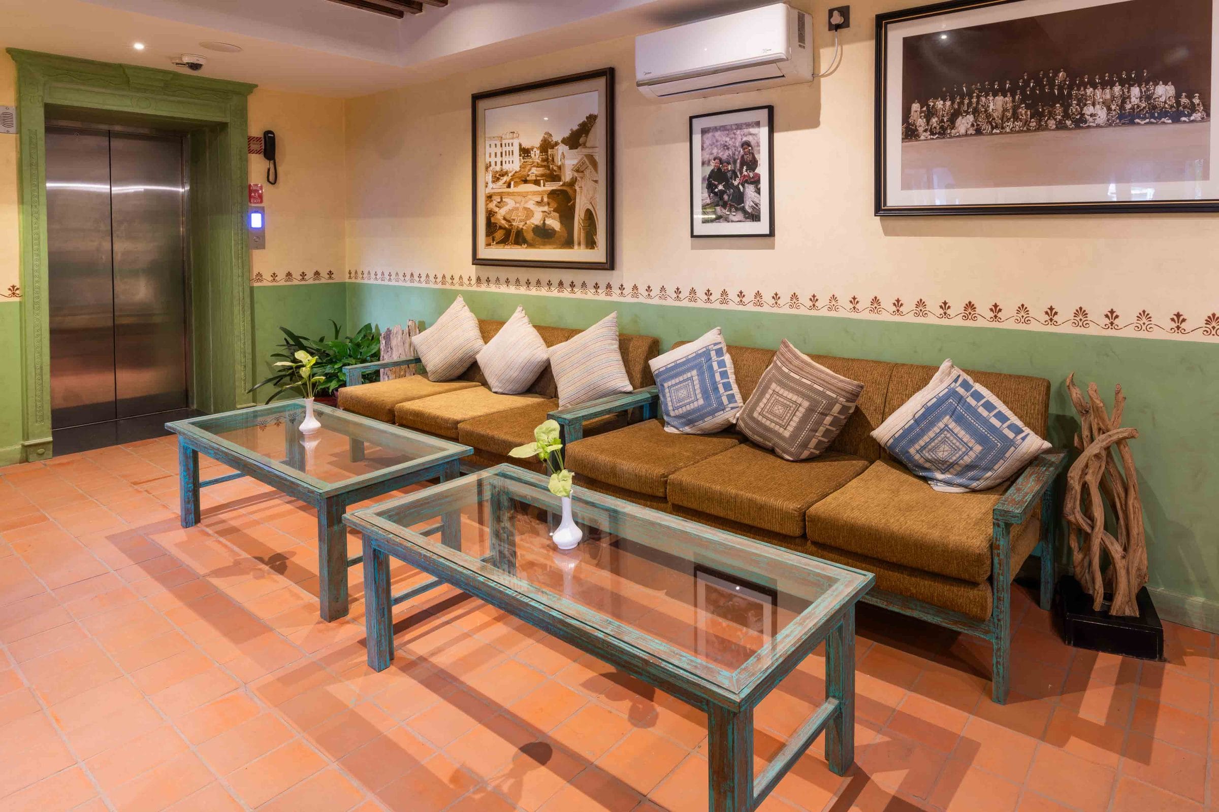 The Seto Ghar lobby lounge at Nepali Ghar Hotel with green wainscoting, hand-stencilled borders, archival photographs, and low seating beside the guest lift.