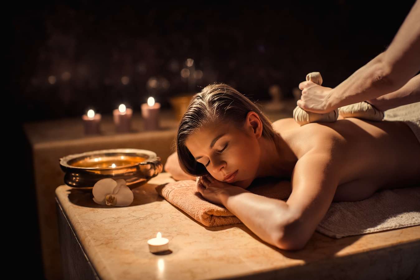 A woman receiving a relaxing massage at YO1, Catskills, New York. Candles and a bowl with flowers are visible in the background, creating a calming ambiance.