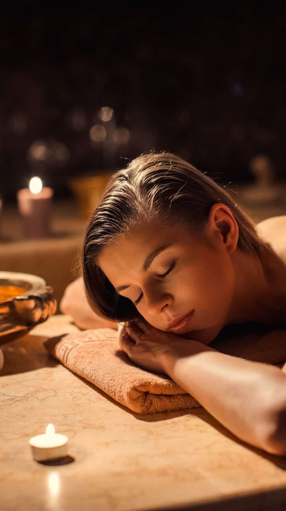 A woman receiving a relaxing massage at YO1, Catskills, New York. Candles and a bowl with flowers are visible in the background, creating a calming ambiance.