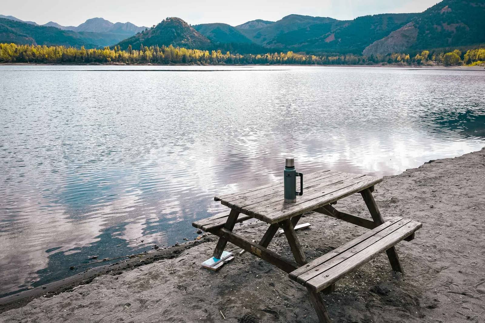 Wooden picnic table with a flask beside a lake (stock image)