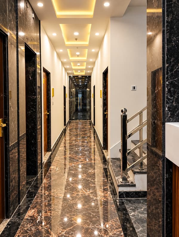 Long guest corridor with a marble floor and cove lighting at Lime Tree Hotel, Vrindavan